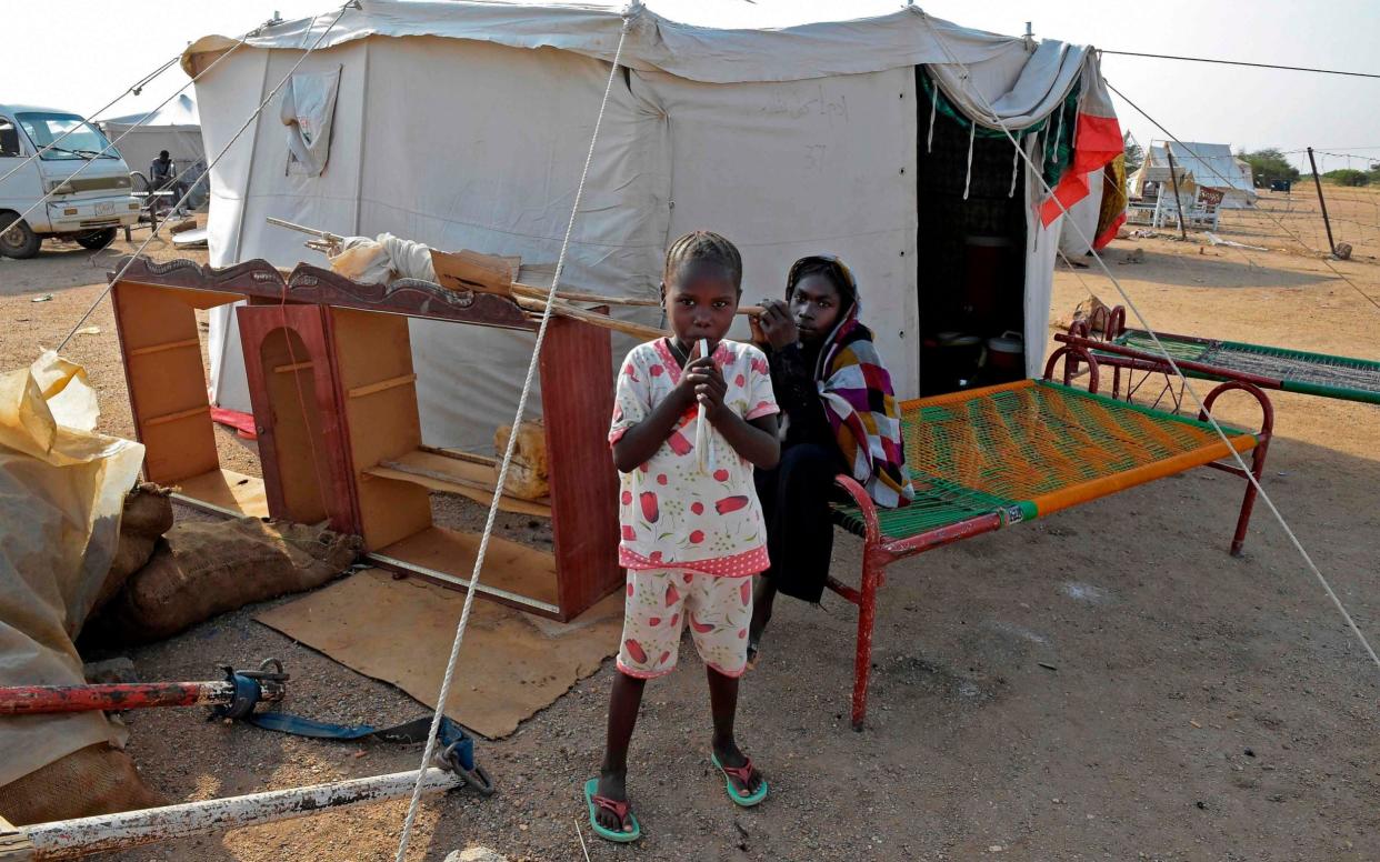 Displaced children stand outside a tent a shelter camp in the village of Tamaniyet, north of Sudan's capital Khartoum - Mazen Mahdi/ AFP