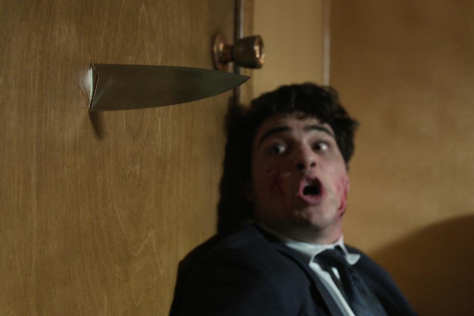 owen crouched behind a door and looking scared at the knife that's pierced through