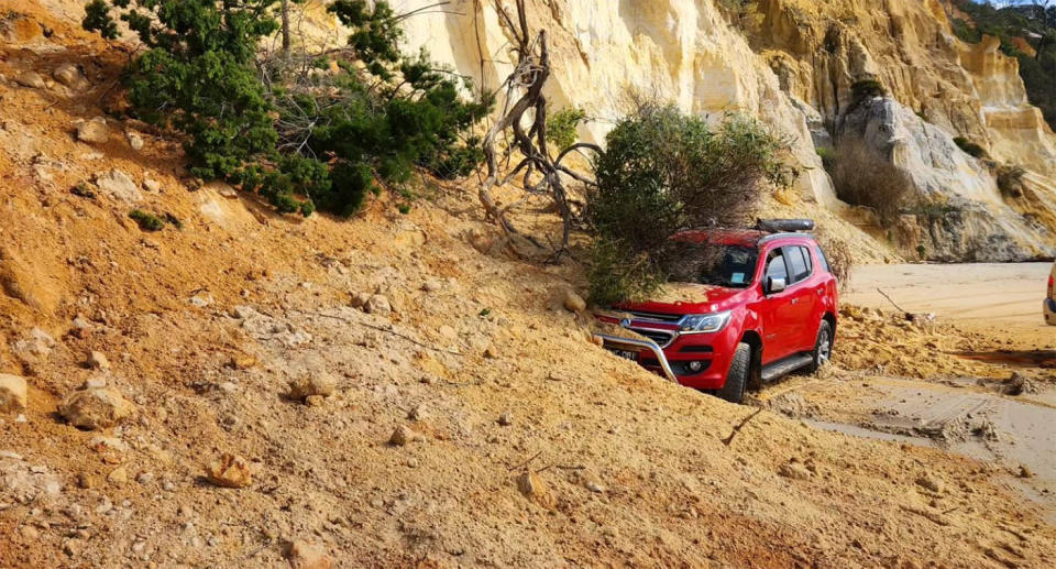 A red Holden 4WD is partially covered by sand and trees following a large land slip on Rainbow Beach