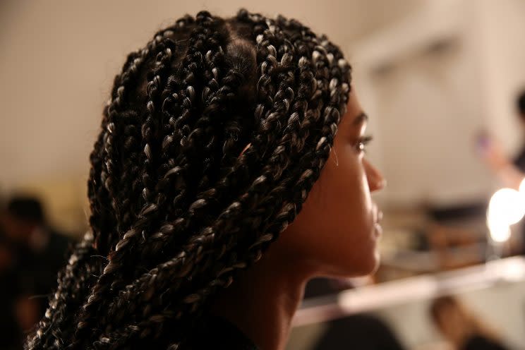 A model poses while hairstylists create box braids.