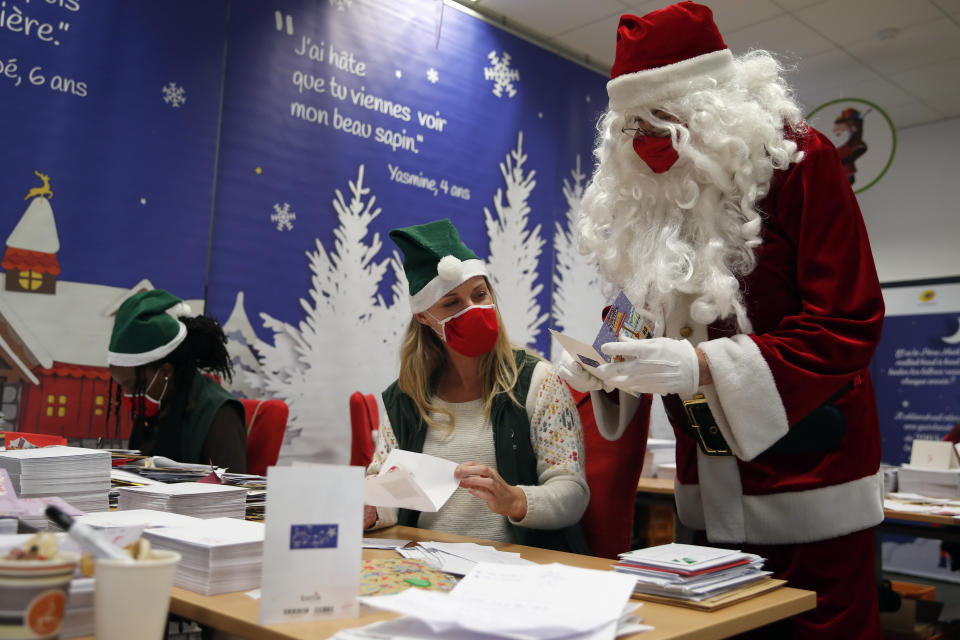 A postal worker dressed as Santa, talks with co-workers who call themselves "Elves" as they open envelopes addressed to "Pere Noel" - Father Christmas in French - in Libourne, southwest France, Monday, Nov. 23, 2020. Letters pouring by the tens of thousands into Santa's mailbox offer a glimpse into the worries and hopes of children awaiting a pandemic-hit Christmas. Along with usual pleas for toys and gadgets, kids are also mailing requests for vaccines, for visits from grandparents, for life to return to the way it was. The office estimates that one letter in three mentions the pandemic. (AP Photo/Francois Mori)