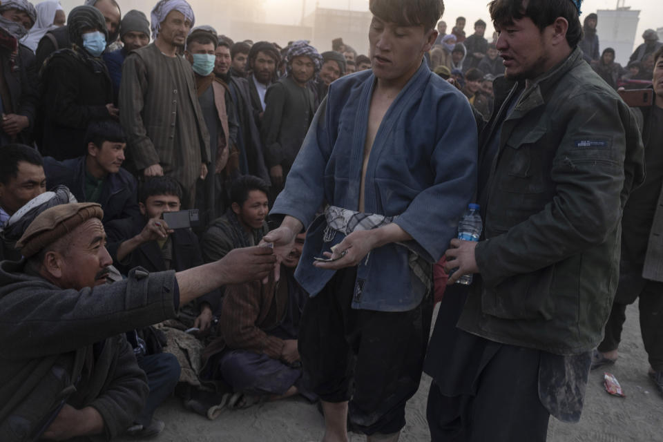 A spectator presses a banknote into the winner's hand after a wresting match in Kabul, Afghanistan, Friday, Dec. 3 , 2021. The scene is one played out each week after Friday prayers in the sprawling Chaman-e-Huzori park in downtown Kabul, where men, mainly from Afghanistan's northern provinces, gather to watch and to compete in pahlawani, a traditional form of wrestling. (AP Photo/ Petros Giannakouris)