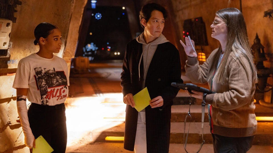 Two actors, Amandla Stenberg (left) and Lee Jung-jae (middle) are looking at showrunner Leslye Headland (right) who is gesturing with her hands and giving directions.