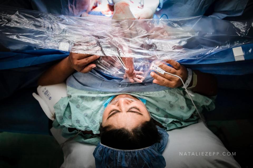 A woman touches her baby's hand through the protective plastic