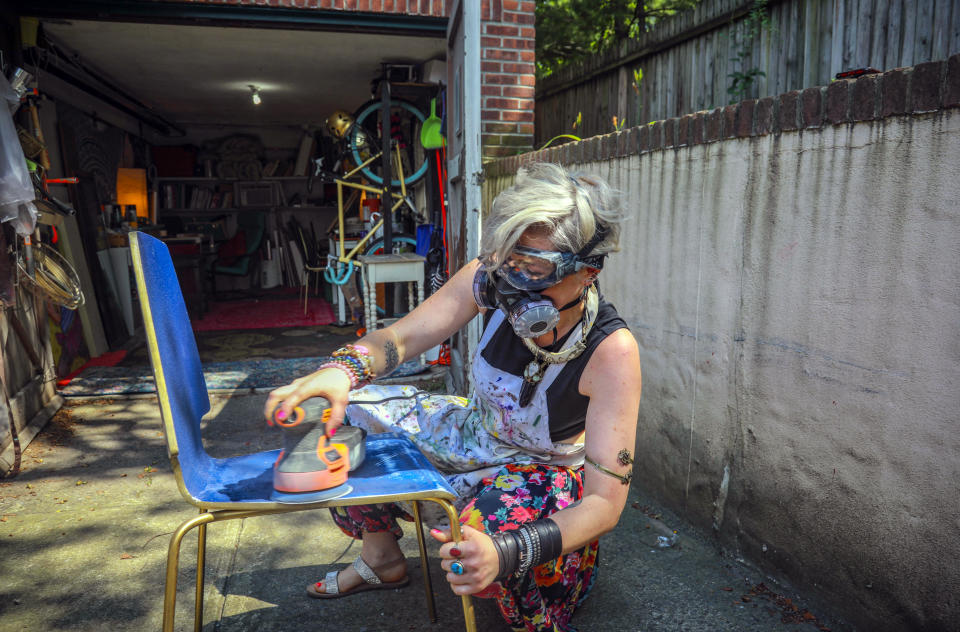 Rachel Berry works in the driveway to her garage studio, refinishing a chair she will turn into art, Monday, July 6, 2020, in New York. Before the coronavirus pandemic, Berry worked as a bartender and waited tables, jobs that gave her enough time to work on her creative pursuits. But as New York City tries to reopen, there's concern that jobs for the city's creative class are no longer readily available. (AP Photo/Bebeto Matthews)