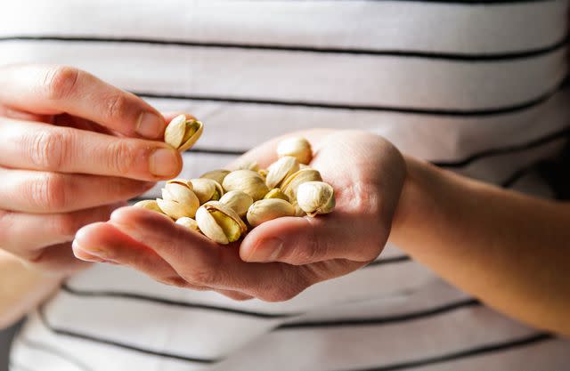 <p>Kinga Krzeminska / Getty Images</p> Person holding handful of pistachios