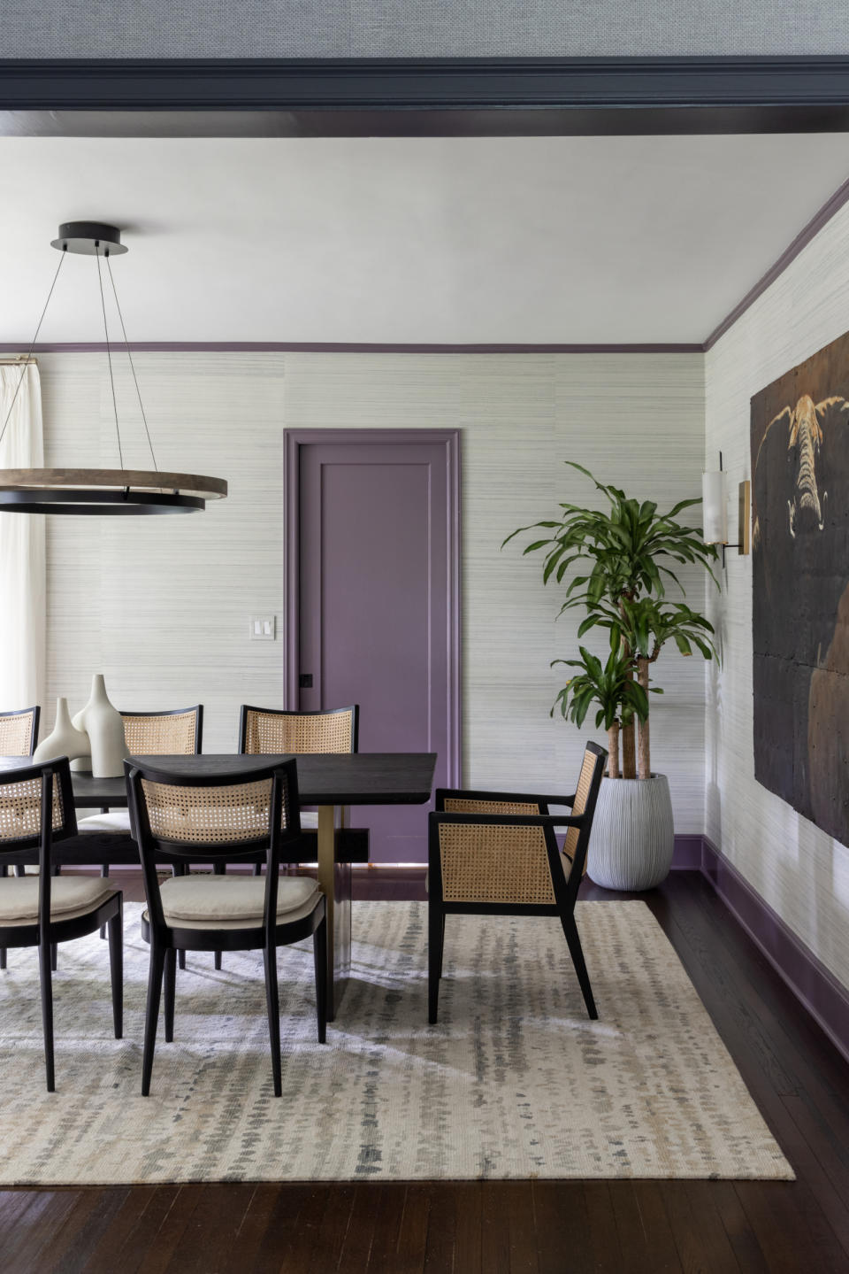 Dining room with dark wood flooring, neutral grasscloth wallpaper, black and cane dining chairs and purple painted woodwork