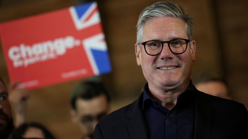 Sir Keir Starmer pictured smiling at a campaign event with a blurred Labour banner saying 'change' in the background 