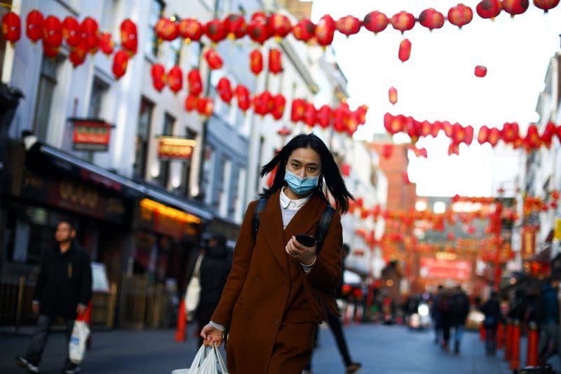 A woman wearing a protective face mask walks in Chinatown district, in London