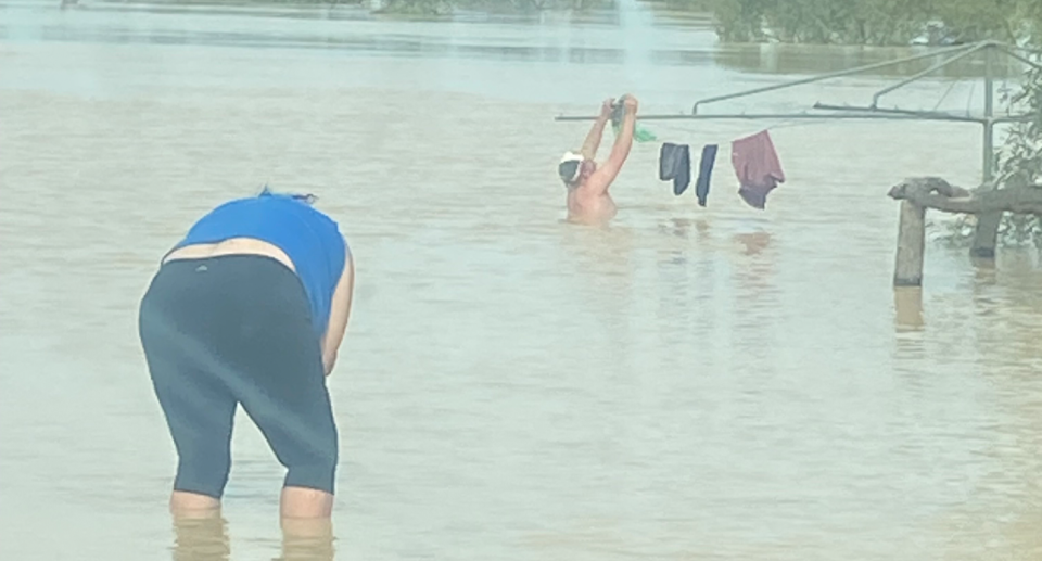 Thiwi Rowlands bends down with the floodwater at her knees to capture the image of Liam hanging washing. 