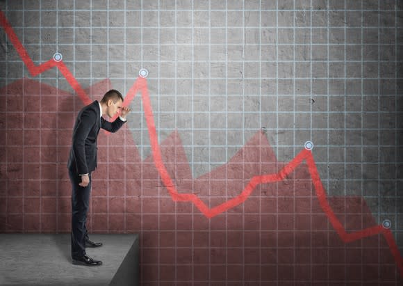 Man in a suit staring down into a drop off with a red downward trending graph in the background.