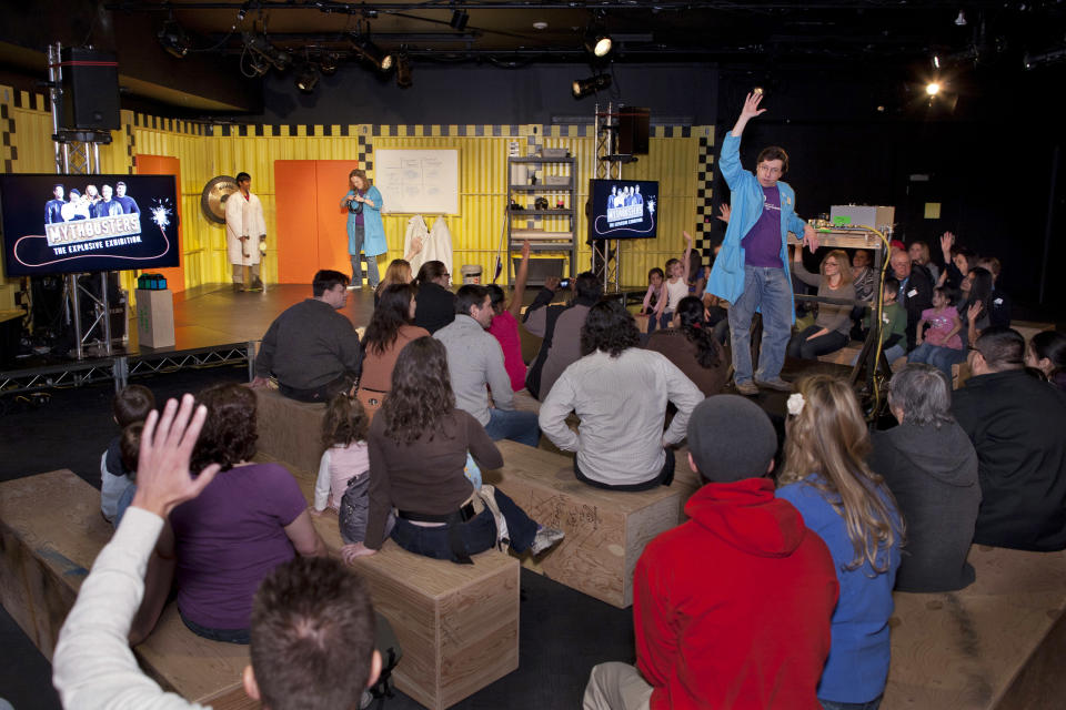 In this March 10, 2012 photo provided by the Museum of Science and Industry, friends and family of museum staff listen to Brett Nicholas, manager of Guest Programs at the Museum of Science and Industry in Chicago asking a question at the Live Demonstration Stage during setup for the show "MythBusters: The Explosive Exhibition," modeled after the Discovery Channel television show "Mythbusters" The exhibit opens Thursday, March 15 and runs through Sept. 3. The planned national tour that will include stops at several other U.S. cities. (AP Photo/Museum of Science and Industry, J.B. Spector)