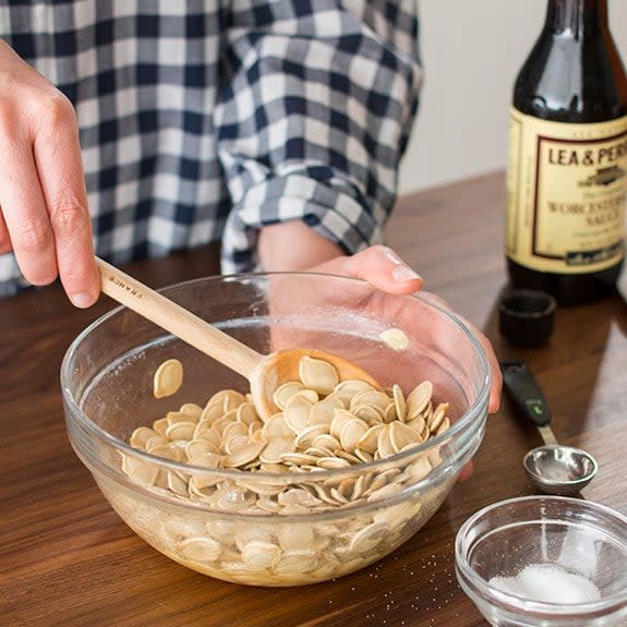 Person stirring seasonings into the seeds with a spatula in a glass bowl