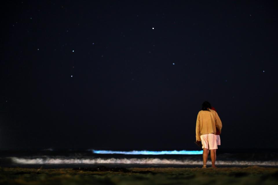 People stand on the beach at night to watch the waves glow blue due to bioluminescence on April 24, 2020 in Newport Beach, California.