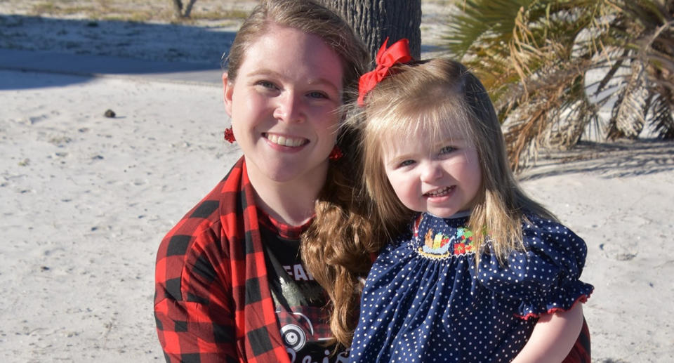 Haley Richardson wearing a red checked shirt holding her daughter Katie smiling at the camera.