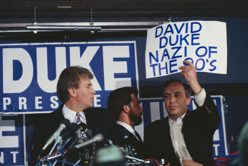 A protester holds up a sign reading, “David Duke Nazi of the 90's,” interrupting David Duke’s speech during a campaign rally.