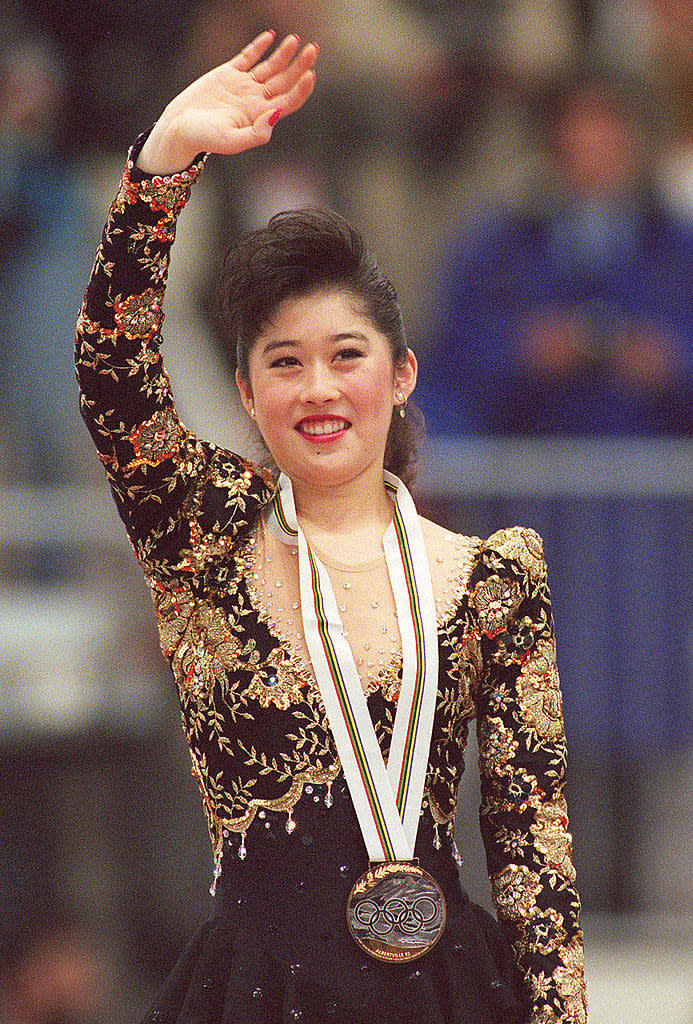 Kristi is waving to the crowd with her gold medal around her neck