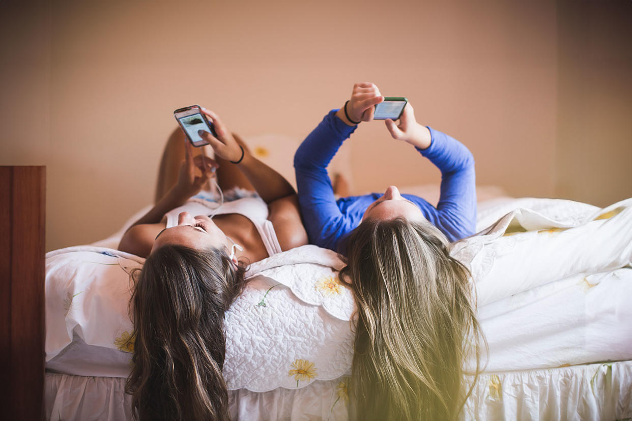 Teenage girls lying on bed looking at smart phones Getty Images/The Good Brigade