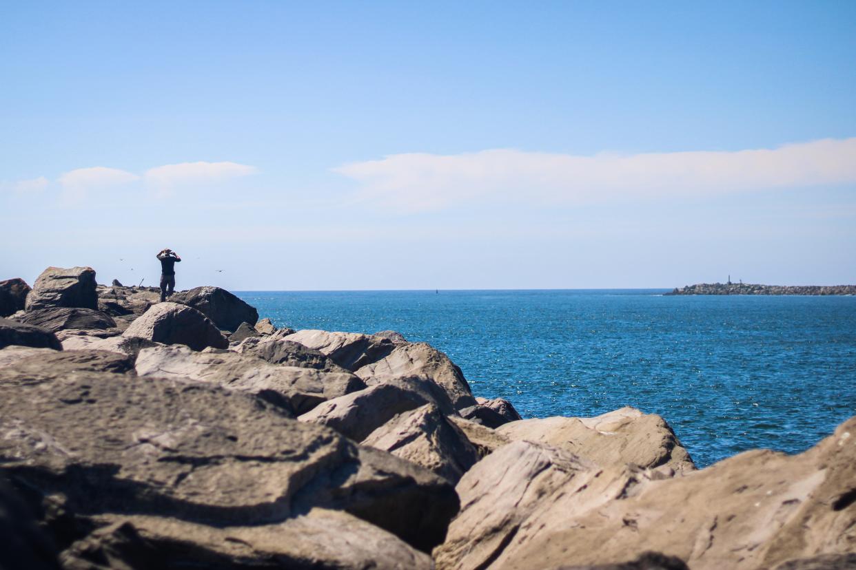 A visitor stands atop the south jetty at the mouth of Tillamook Bay and takes a photo July 28, 2023. The north jetty sits across the way from the Bayocean Spit.