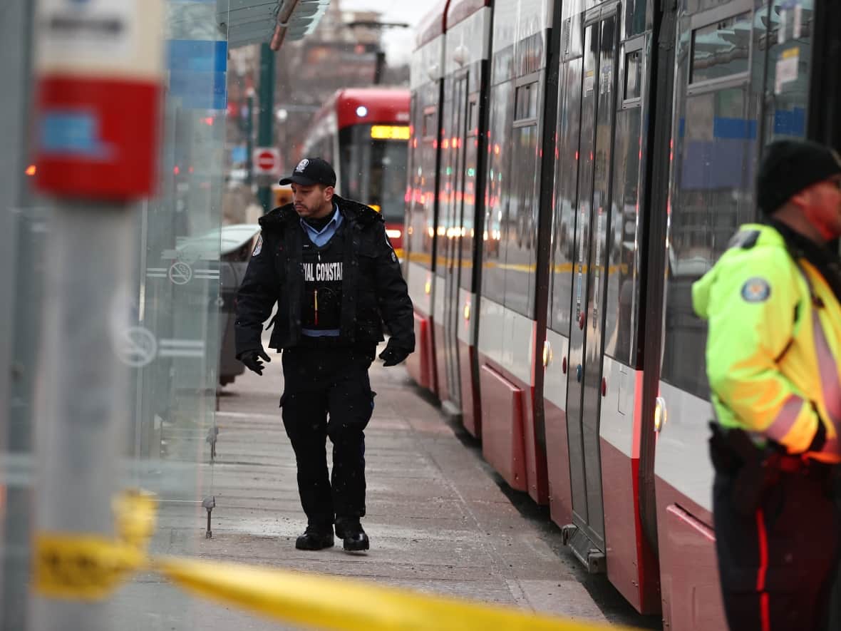 A TTC special constable walks alongside a streetcar where a woman in her 20s was stabbed several times on Tuesday. A suspect was arrested and the victim taken to hospital with serious but non-life-threatening injuries. (Evan Mitsui/CBC - image credit)
