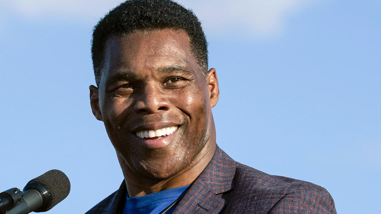 Georgia Republican Senate candidate Herschel Walker smiles in front of a microphone.