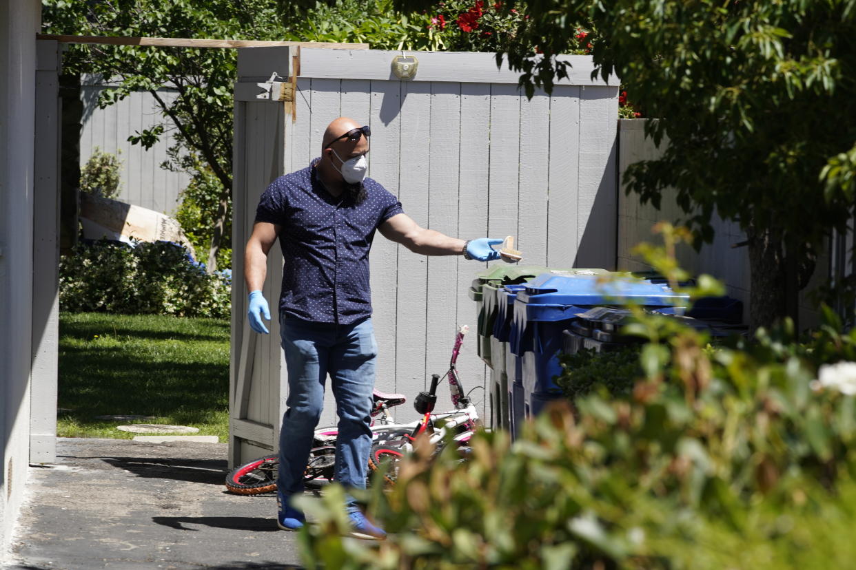 An unidentified man puts a wooden bath brush in the trash can at a ranch-style house in the West Hills neighborhood of the San Fernando Valley in Los Angeles, Monday, May 9, 2022. Police say three children were found dead at the home over the weekend and their mother and a teenager were arrested in the killings. (AP Photo/Damian Dovarganes)