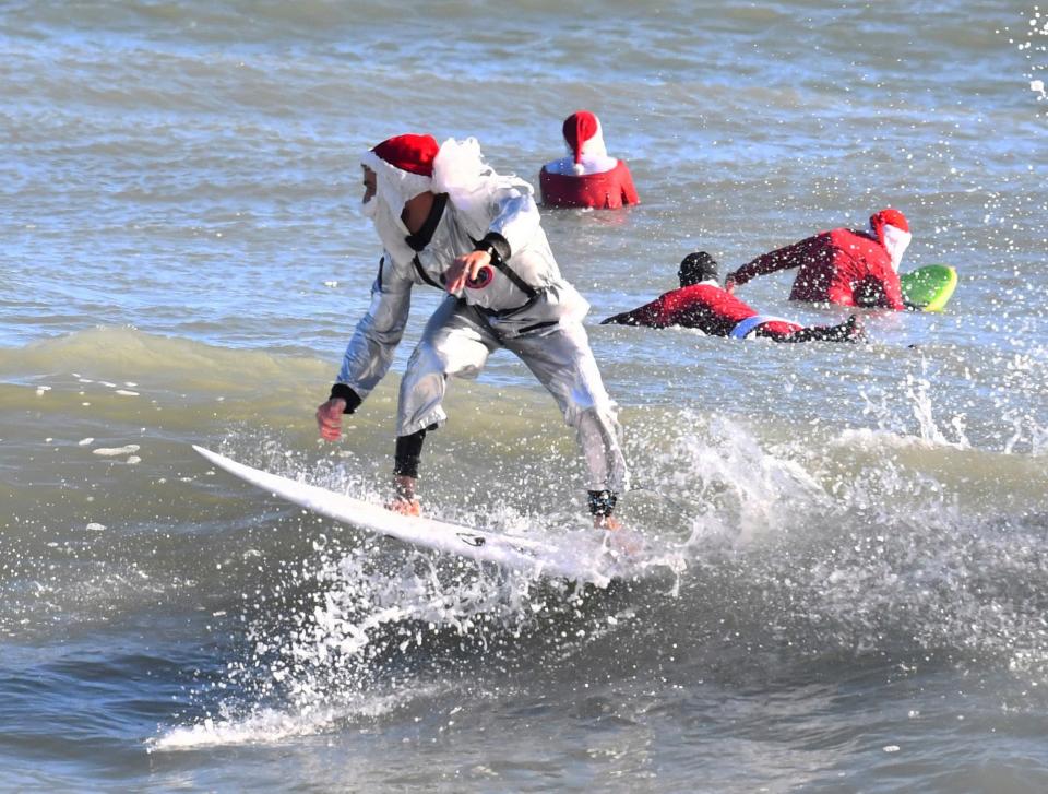 Surfer Corey Howell in a space man Surfing Santa suit, rides with waves with other surfing Santas for the 14th annual Surfing Santas of Cocoa Beach event Christmas Eve morning, Saturday, Dec. 24, 2022 (AP)