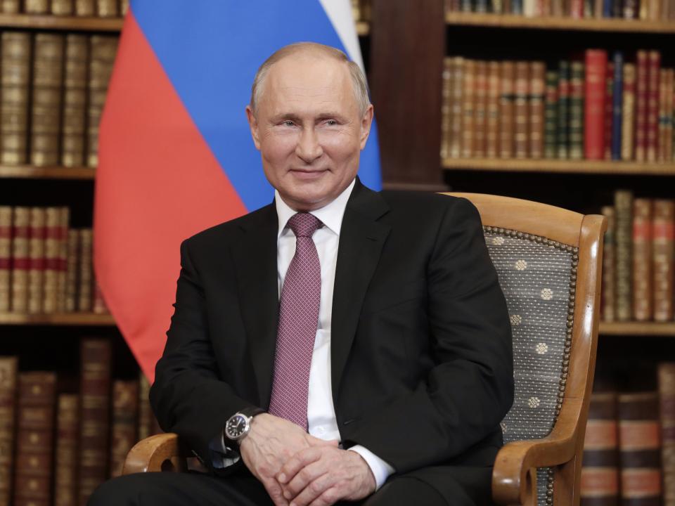 Vladimir Putin sits and smiles.