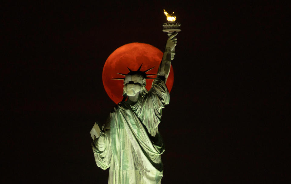 blood red full moon in the background and the top half of the statue of liberty in the foreground.