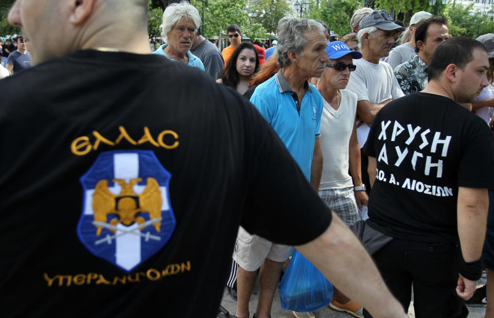 People wait in a line as members of Greece's extreme right Golden Dawn party hand out food at Athens' main Syntagma Square, opposite parliament, on Wednesday, Aug. 1, 2012. The volunteers checked ID cards of the public before handing Greek citizens food that included milk cartons, pasta, potatoes and olive oil. Golden Dawn won 18 seats in the 300-seat parliament in June general elections. Senior party members openly support a policy of granting Greek citizenship based on racial identity. The party has stepped up its charity effort as Greece is suffering through a fifth year of recession, with rapidly rising rates of poverty and unemployment. The T-shirts, left, read ''Greece, Above all'' and ''Golden Dawn.'' (AP Photo/Thanassis Stavrakis)