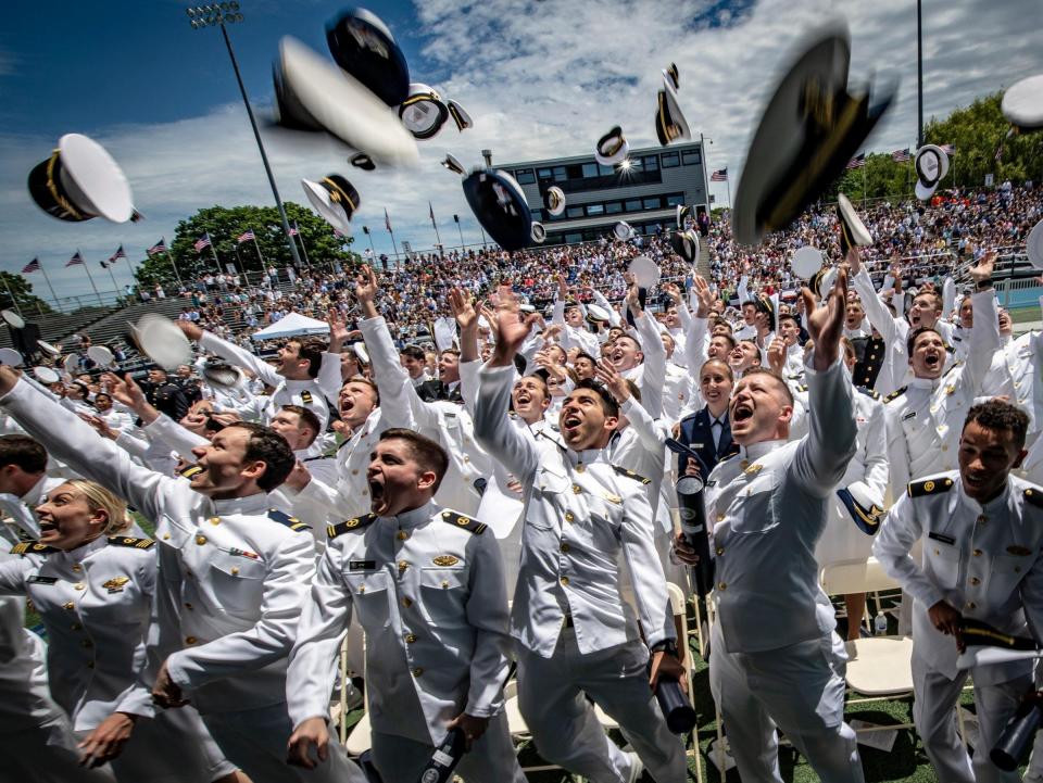 A crowd of people, wearing white uniforms, throw their hats in the air in celebration.
