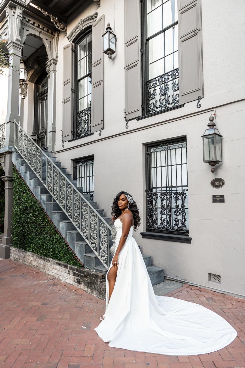 A bride stands in a strapless wedding dress with a slit in front of a staircase.