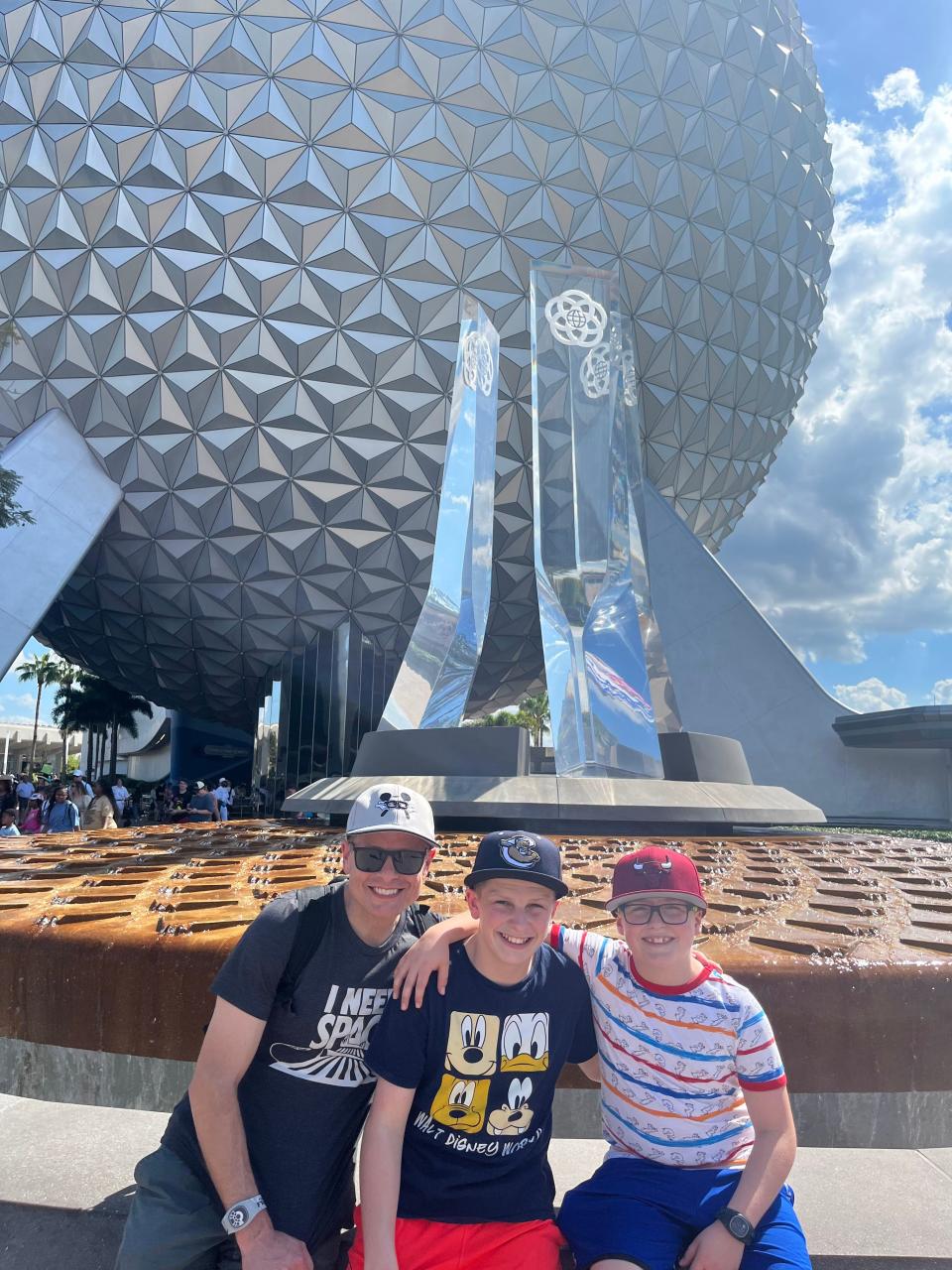 kari's husband and sons posing for a photo in front of the epcot ball in epcot at disney world