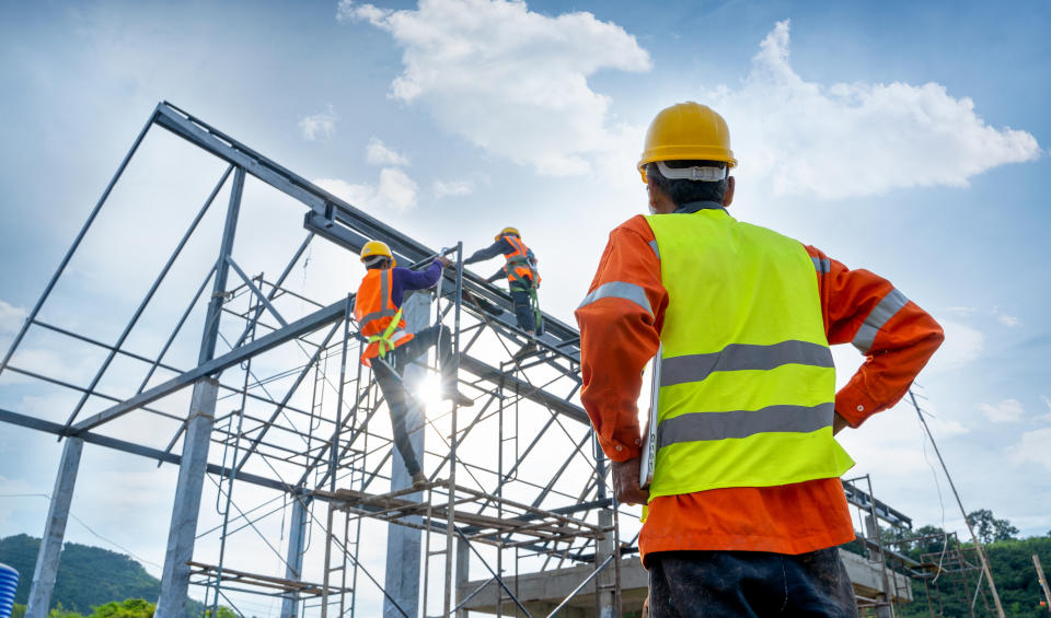 Engineer technician watching team of workers on high steel platform,Engineer technician Looking Up and Analyzing an Unfinished Construction Project.