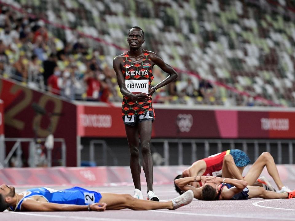 Kenya's Abraham Kibiwot stands after the steeplechase while runners lay on the ground.