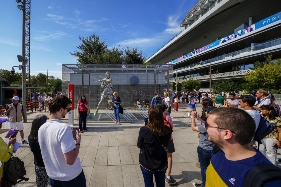 Aficionados se sacan fotos frente a la estatua de Rafael Nadal en el estadio Roland Garros durante el torneo de tenis de los Juegos Olímpicos de París, el domingo 28 de julio de 2024, en París. (AP Foto/Manu Fernández)