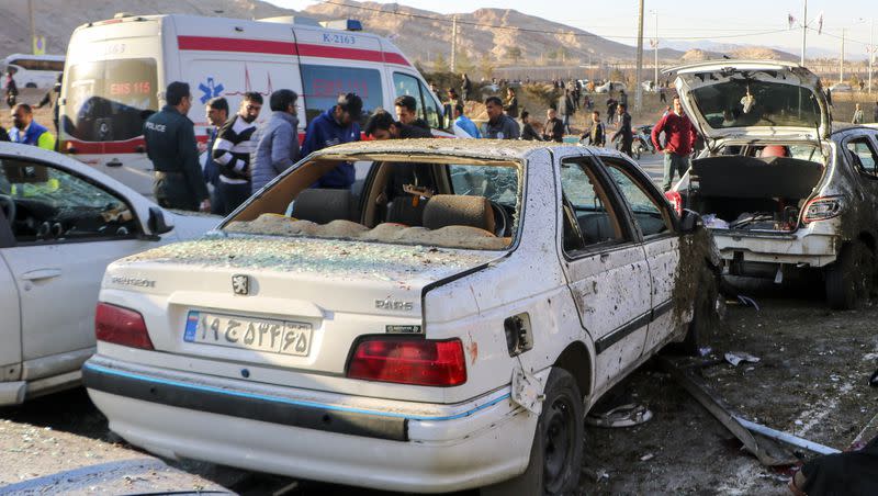 People stay next to destroyed cars after an explosion in Kerman, Iran, on Wednesday, Jan. 3, 2024. Iran says bomb blasts at an event honoring a prominent Iranian general slain in a U.S. airstrike in 2020 have killed at least 103 people and wounded 188 others.