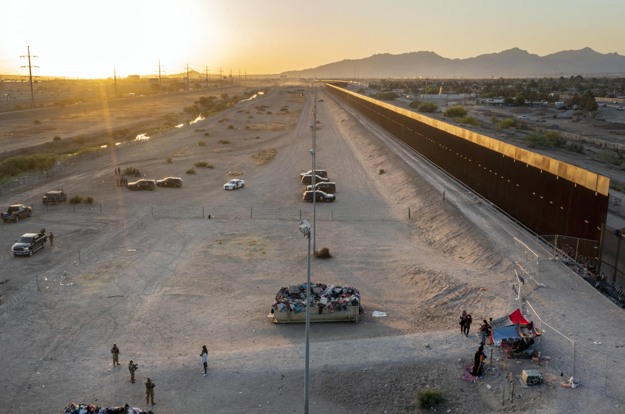 A small group of migrants, bottom right, are pictured while camping outside a gate in the border fence in El Paso, Texas, Friday, May 12, 2023. The border between the U.S. and Mexico was relatively calm Friday, offering few signs of the chaos that had been feared following a rush by worried migrants to enter the U.S. before the end of pandemic-related immigration restrictions. (AP Photo/Andres Leighton)
