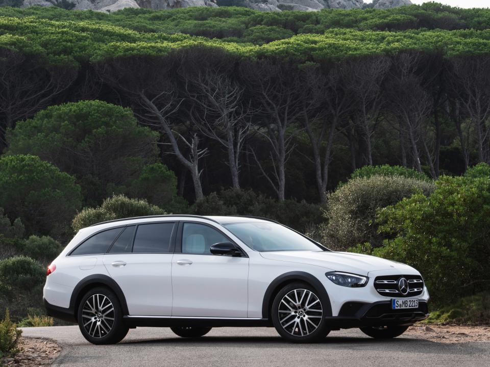 A white Mercedes-Benz wagon parked on pavement in front of greenery.