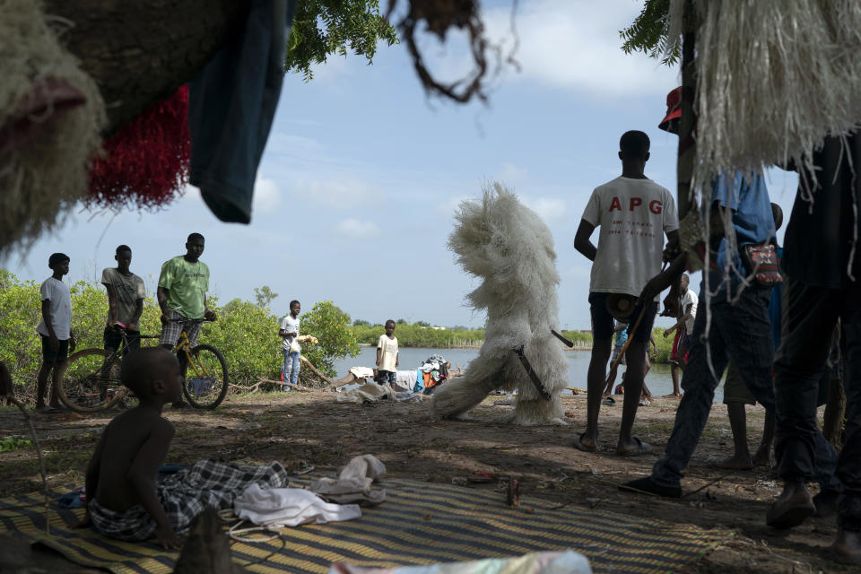 Holding two machetes, a man dressed as the Kankurang walks past a boy, left bottom, who is taking part in the initiation rites, during a Mandinka ritual in Serrekunda, Gambia, Saturday, Sept. 25, 2021. The Kankurang rite was recognized in 2005 by UNESCO, which proclaimed it a cultural heritage. Despite his fearsome appearance, the Kankurang symbolizes the spirit that provides order and justice and is considered a protector against evil. He appears at ceremonies where circumcised boys are taught cultural practices, including discipline and respect. (AP Photo/Leo Correa)