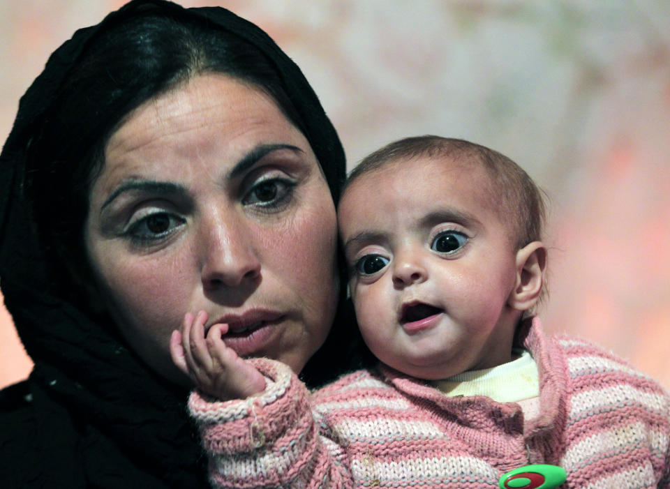 In this Tuesday, March 11, 2014 photo, Mervat, 31, speaks during an interview with The Associated Press as she holds her 9-month-old daughter Shurouk inside their tent camp for Syrian refugees camp in Kab Elias, in Lebanon's Bekaa Valley. Trapped in her northern Syrian village by fighting, Mervat watched her newborn baby progressively shrink. Her daughter’s dark eyes seemed to grow bigger as her face grew more skeletal. Finally, Mervat escaped to neighboring Lebanon, and a nurse told her the girl was starving. Such stark malnutrition was rare in Syria in the past, but as the country’s conflict enters its fourth year, international aid workers fear malnutrition is rising among children in Syria and among refugees amid the collapse in the health care system. (AP Photo/Bilal Hussein)