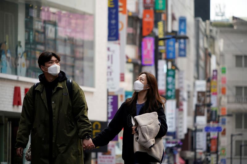 A couple wearing masks to prevent contracting the coronavirus walks on an empty street at a shopping district in Seoul