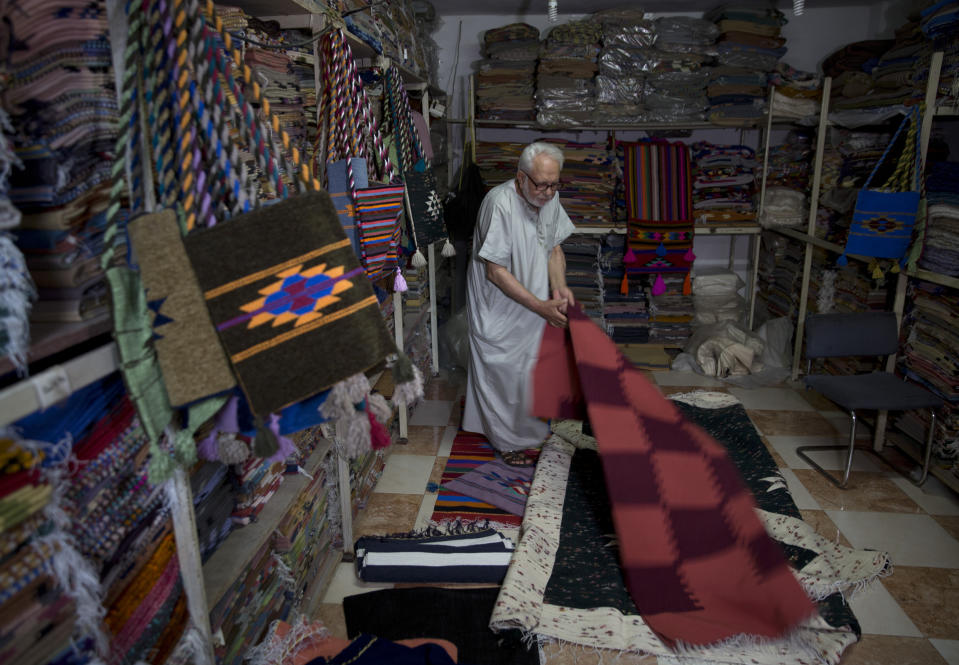 In this Saturday, July 6, 2019 photo, Palestinian Mahmoud al-Sawwaf, the owner of a traditional carpets factory, displays his products in Gaza City.Talk about old Gaza, and what pops up are images of clay pottery, colorful glassware, bamboo furniture and ancient frame looms weaving bright rugs and mats. As such professions could be dying worldwide, the pace of their declining is too fast in Gaza that out of its some 500 looms, only one is still functioning. (AP Photo/Khalil Hamra)