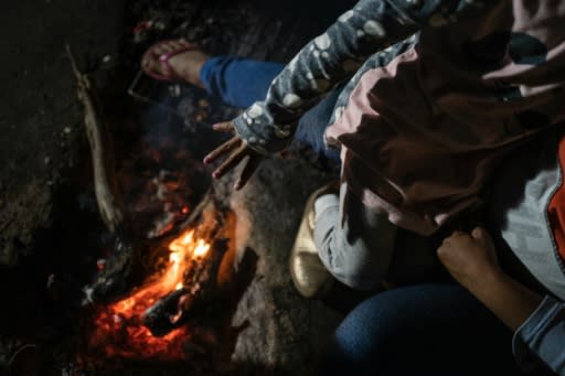 A girl from Guerrero State warms her hand over the campfire in her family's campsite in Chamizal Park in Ciudad Juarez, Mexico