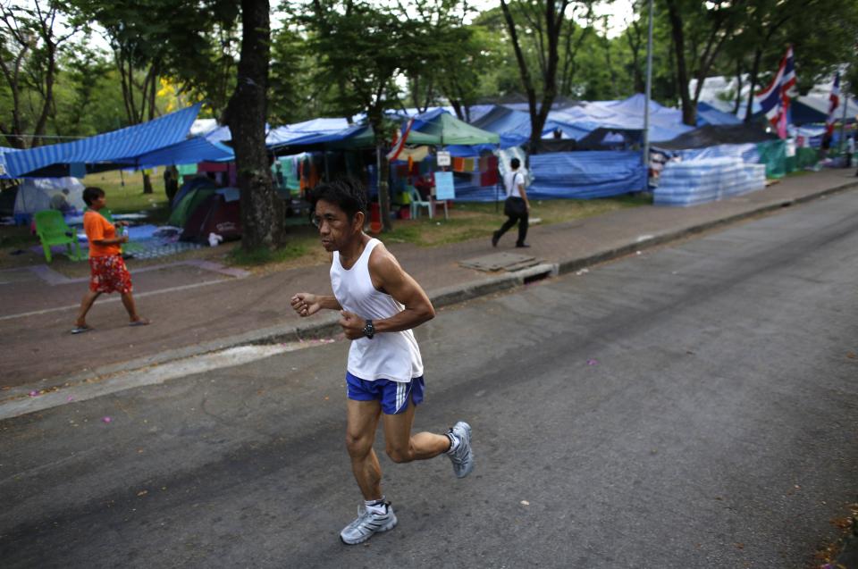 A jogger runs past tents set up by anti-government protesters at Lumpini Park in downtown Bangkok April 7, 2014. Viewed from above, with it's sea of blue tarpaulin sheets, Bangkok's Lumpini Park looks like a shelter for victims of a natural disaster. Surrounded by skyscrapers and once a haven for joggers, the Thai capital's most famous park has become the temporary home of more than 10,000 supporters of a movement that's been trying for five months to bring down Prime Minister Yingluck Shinawatra. Picture taken April 7, 2014. REUTERS/Darren Whiteside (THAILAND - Tags: POLITICS CIVIL UNREST)
