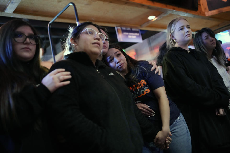 Bryanna Saiz, center, cries with others during a memorial for Jackson Zinn at a Texas Roadhouse restaurant, Thursday, March 17, 2022, in Hobbs, New Mexico. Zinn, who worked at the restaurant, was killed with several other student golfers and the coach of University of the Southwest in a crash in Texas. (AP Photo/John Locher)