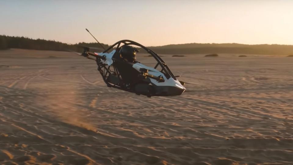 A Jetson One all-electric personal aircraft hovering over a sandy beach at sunset.