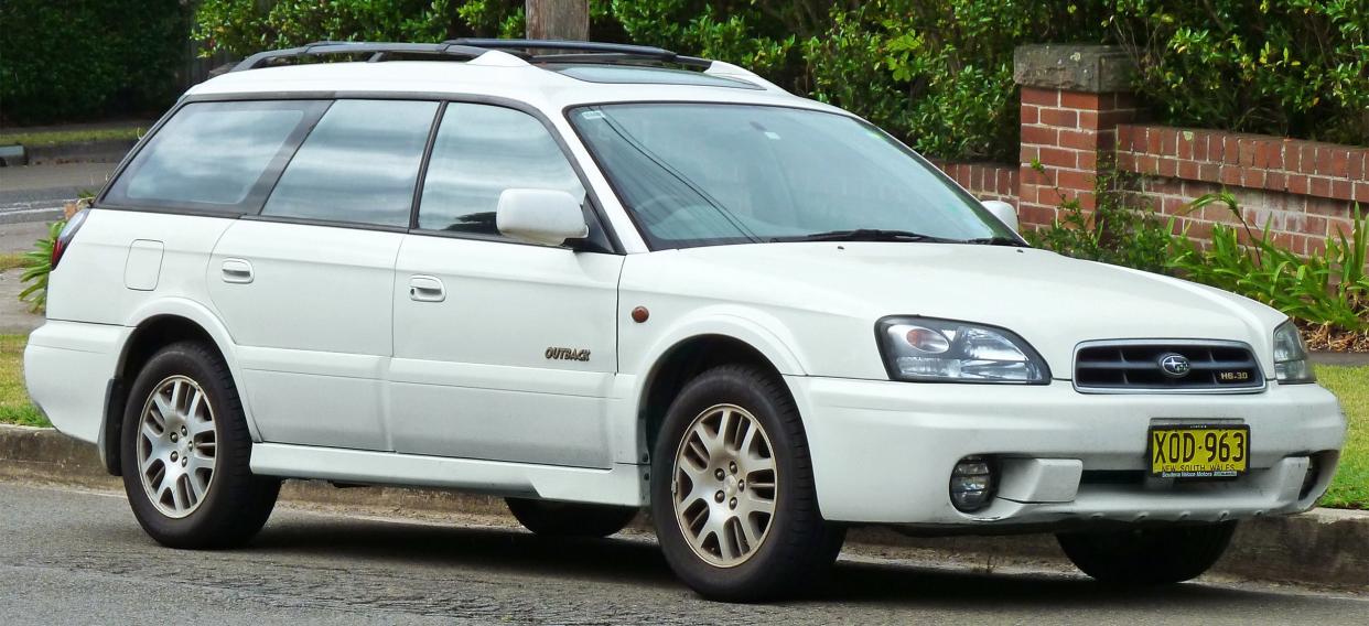 White Second-Generation Subaru Outback parked on street in summer.