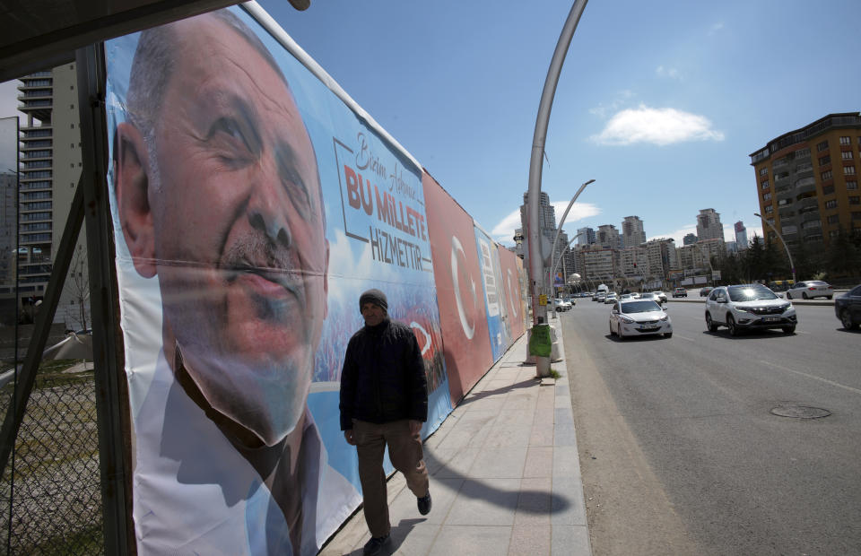 A man walks by huge posters of Turkey's President Recep Tayyip Erdogan, still displayed despite an election ban, near a polling station during the local elections in Ankara, Turkey, Sunday, March 31, 2019. Turkish citizens have begun casting votes in municipal elections for mayors, local assembly representatives and neighborhood or village administrators that are seen as a barometer of Erdogan's popularity amid a sharp economic downturn. (AP Photo/Burhan Ozbilici)