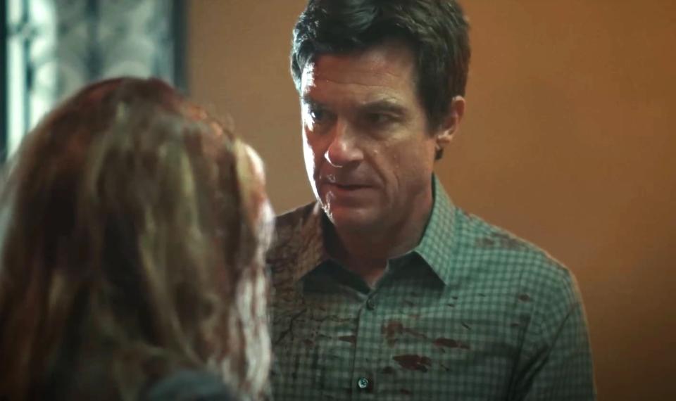 Jason Bateman, in a checked shirt with blood stains, stares intently at another person with her back turned in a tense scene